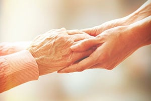 two sets of hands, a caregiver helping a senior to stand
