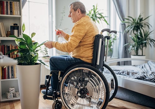 A man in a wheelchair watering his indoor plant | Modern Mobility Solutions